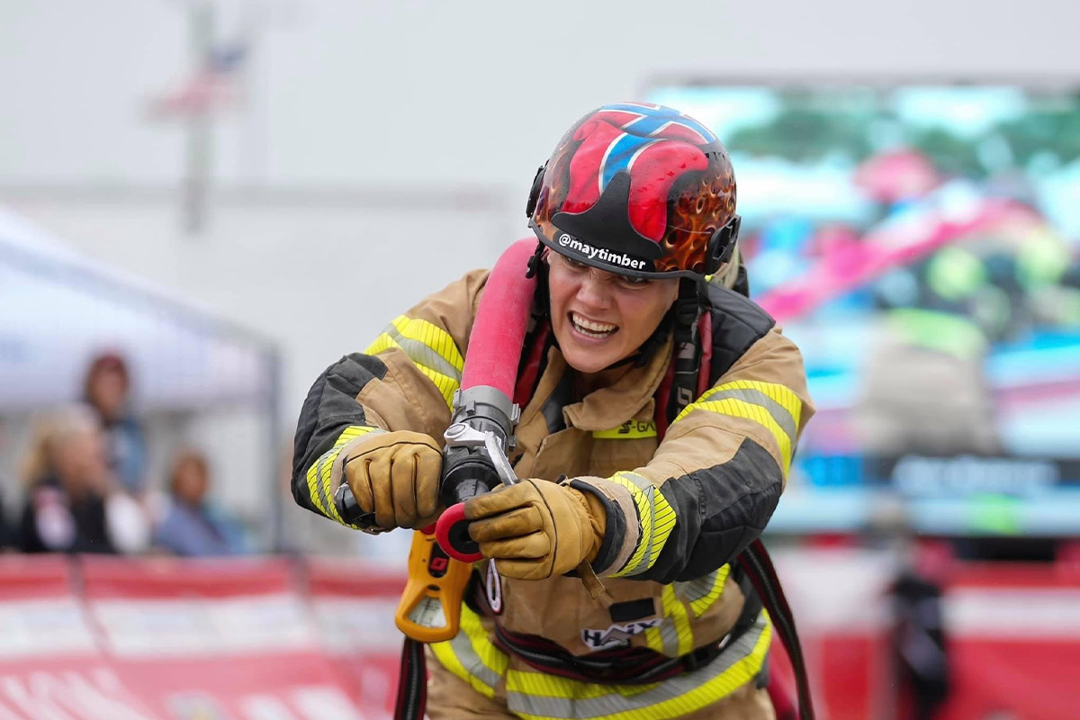 Feuerwehrfrau May bei ihrem Lauf in voller Montur und Feuerwehrschlauch über der Schulter