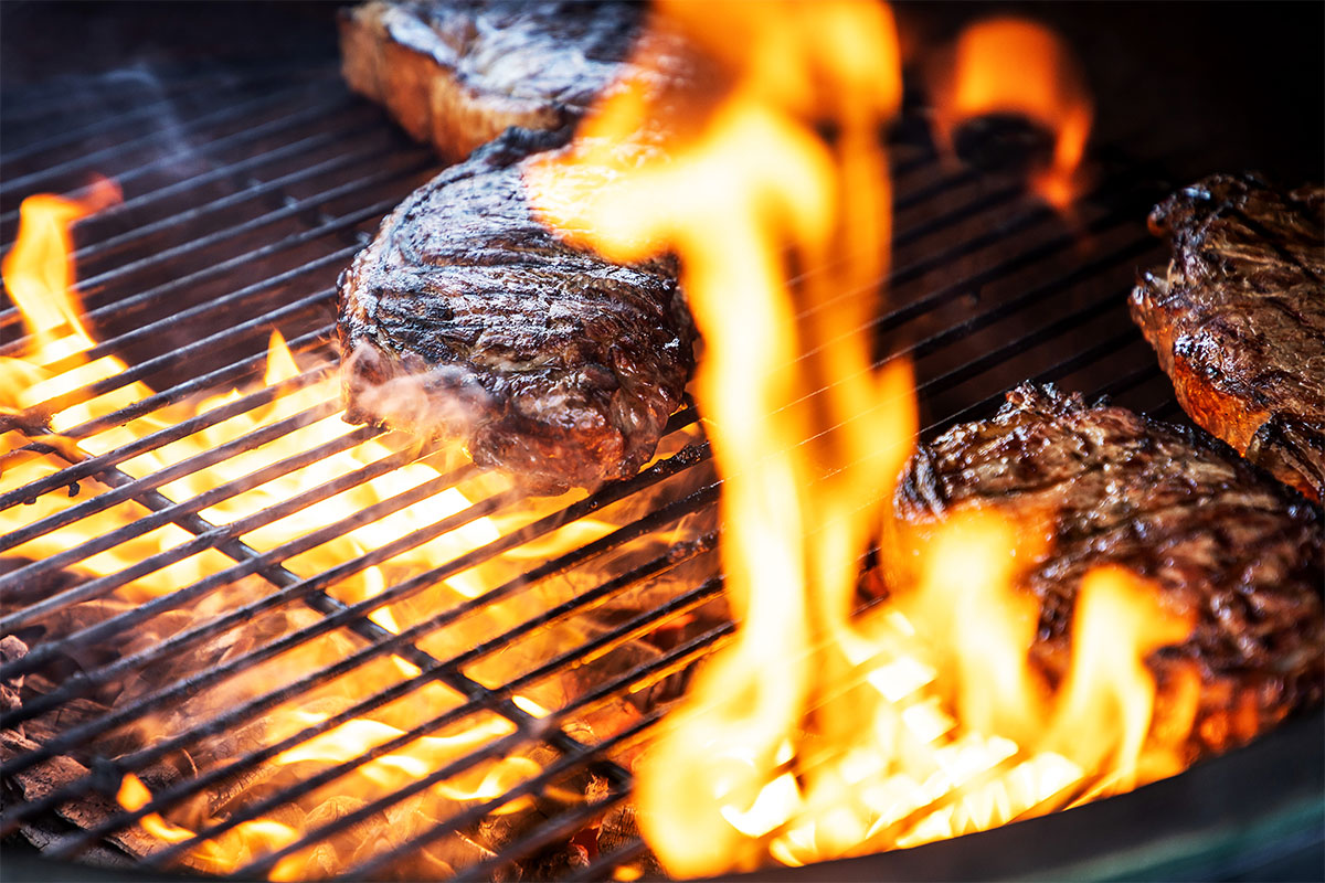 Flammen lodern um die Steaks auf dem Grillrost