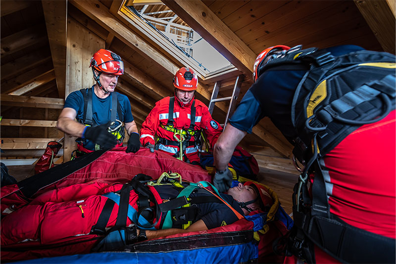 Drei Feuerwehrmänner packen einen Kameraden in den Rettungssack